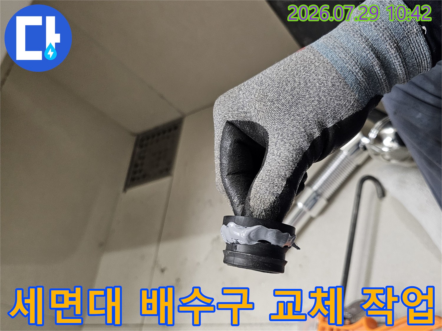 장갑을 낀 손으로 세면대 하부 배수 트랩과 연결 부위를 점검하는 모습