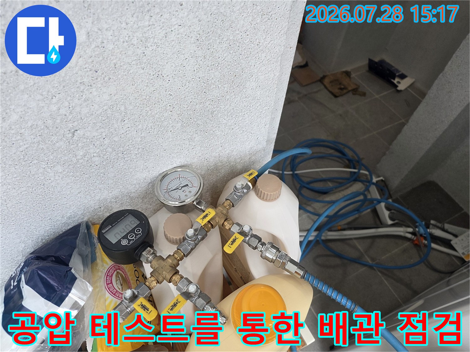다용도실 내부 수도 배관에 공압 검사 장치를 연결하여 누수 여부를 확인하는 전문적인 과정