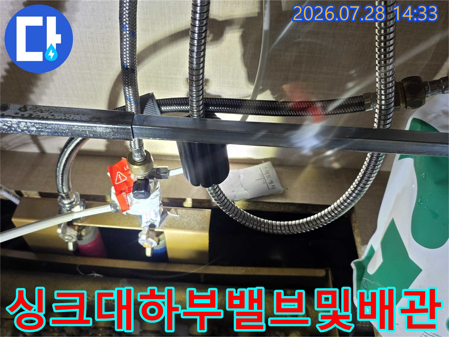 붉은색 핸들 밸브가 부착된 싱크대 하단 배관 분배기와 주름 호스들의 연결 모습