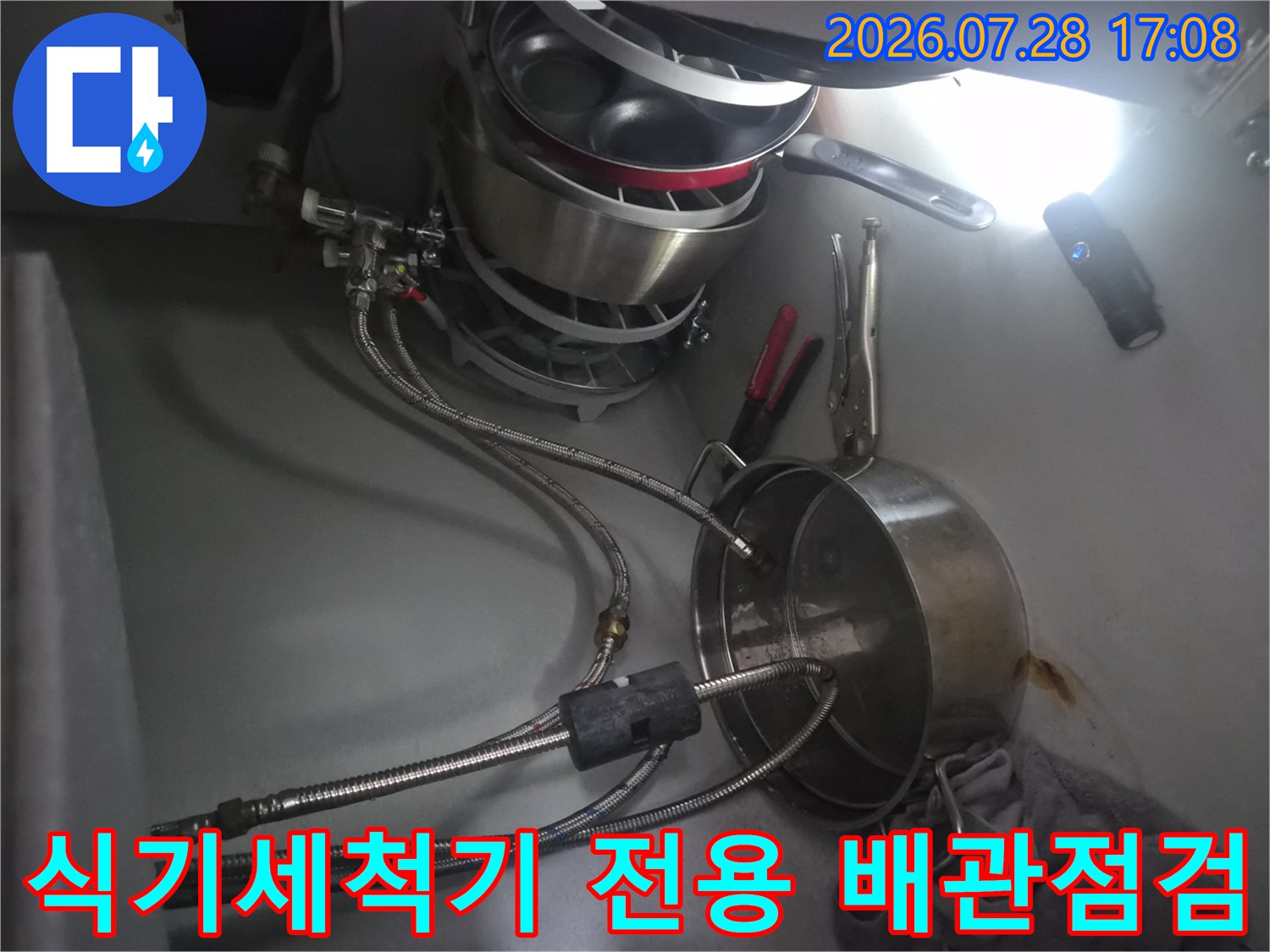 싱크대 아래쪽 식기세척기 연결 부품과 호스 구간을 정밀하게 점검하는 사진