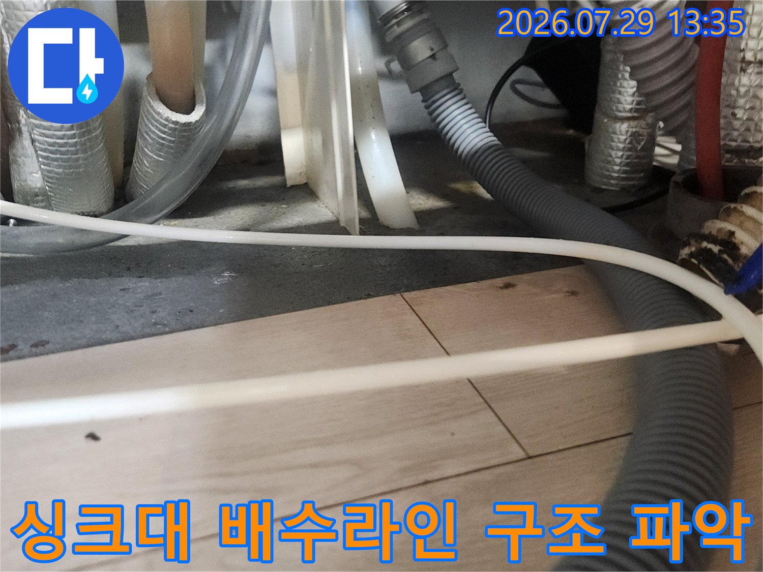 다양한 소재의 보호재와 호스가 얽힌 싱크대 하부의 복잡한 관로