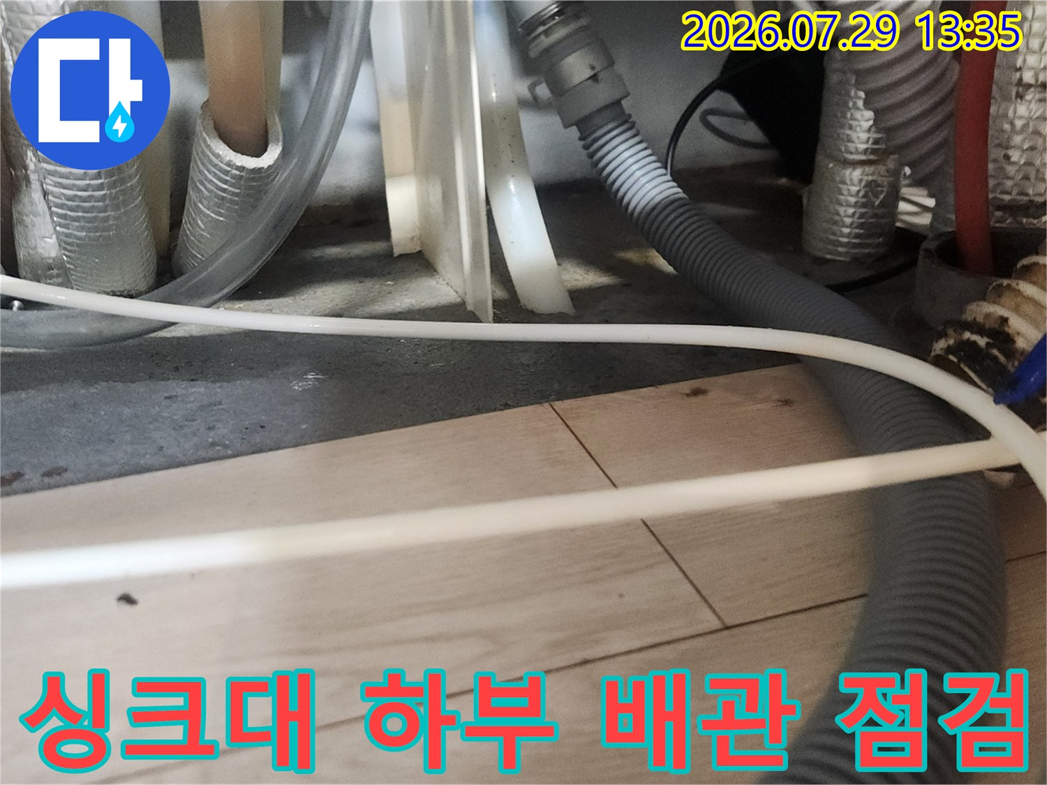 싱크대 아래쪽에 노출된 회색 배관과 연결 부위를 정밀하게 점검하는 현장 모습입니다.