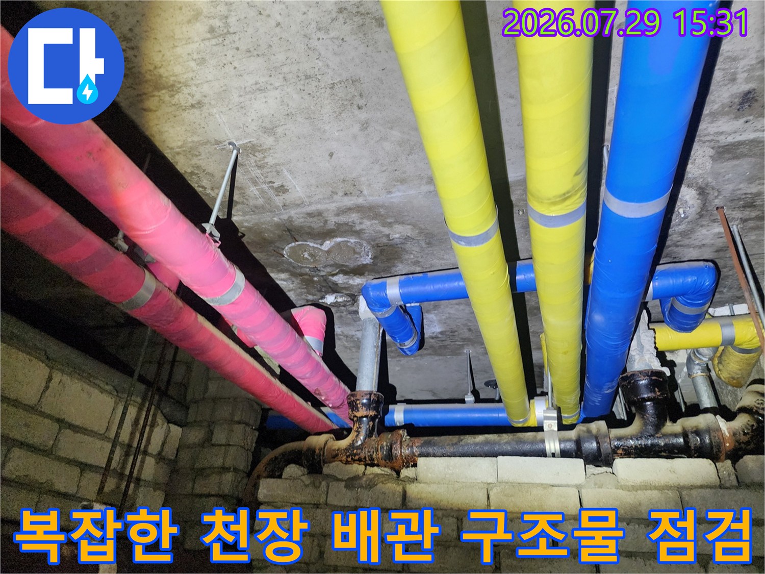 천장 안쪽에 노란색과 분홍색 그리고 파란색으로 구분된 여러 가닥의 배관이 뻗어 있는 모습