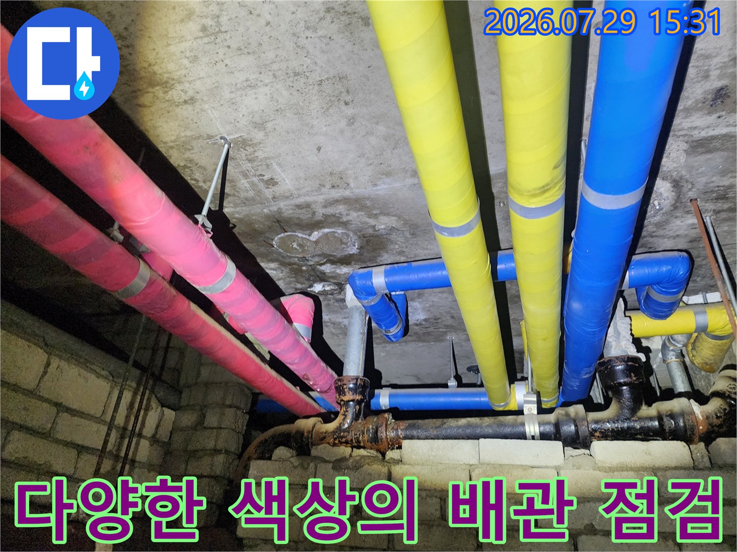화장실 천장 내 노란색과 분홍색 보온재로 감싸진 복잡한 배관망