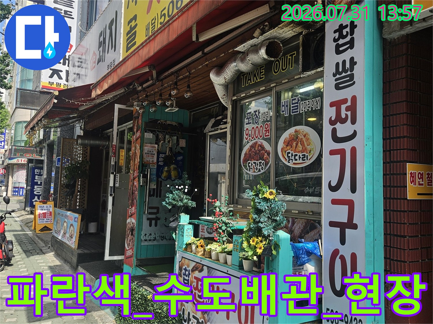 상가 외벽에 설치된 파란색 배관과 안내문이 붙은 현장 사진