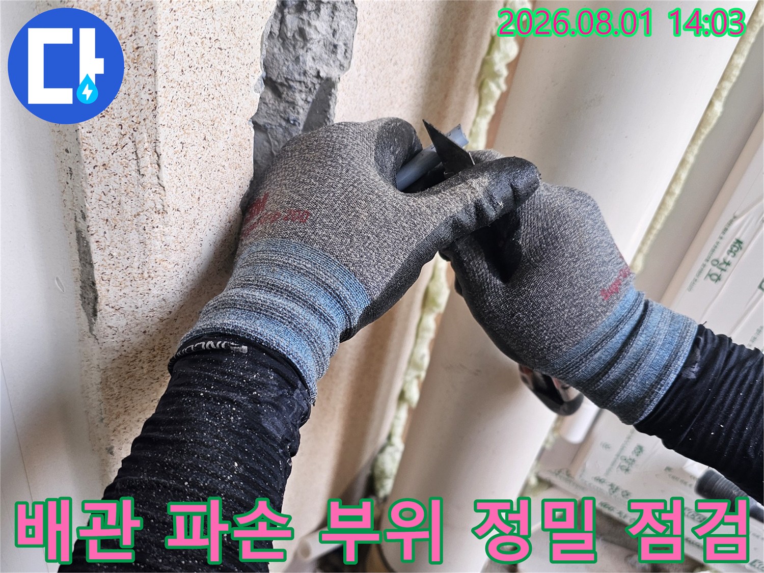 장갑을 낀 작업자가 세탁실 벽면의 손상된 배관을 검사하는 장면