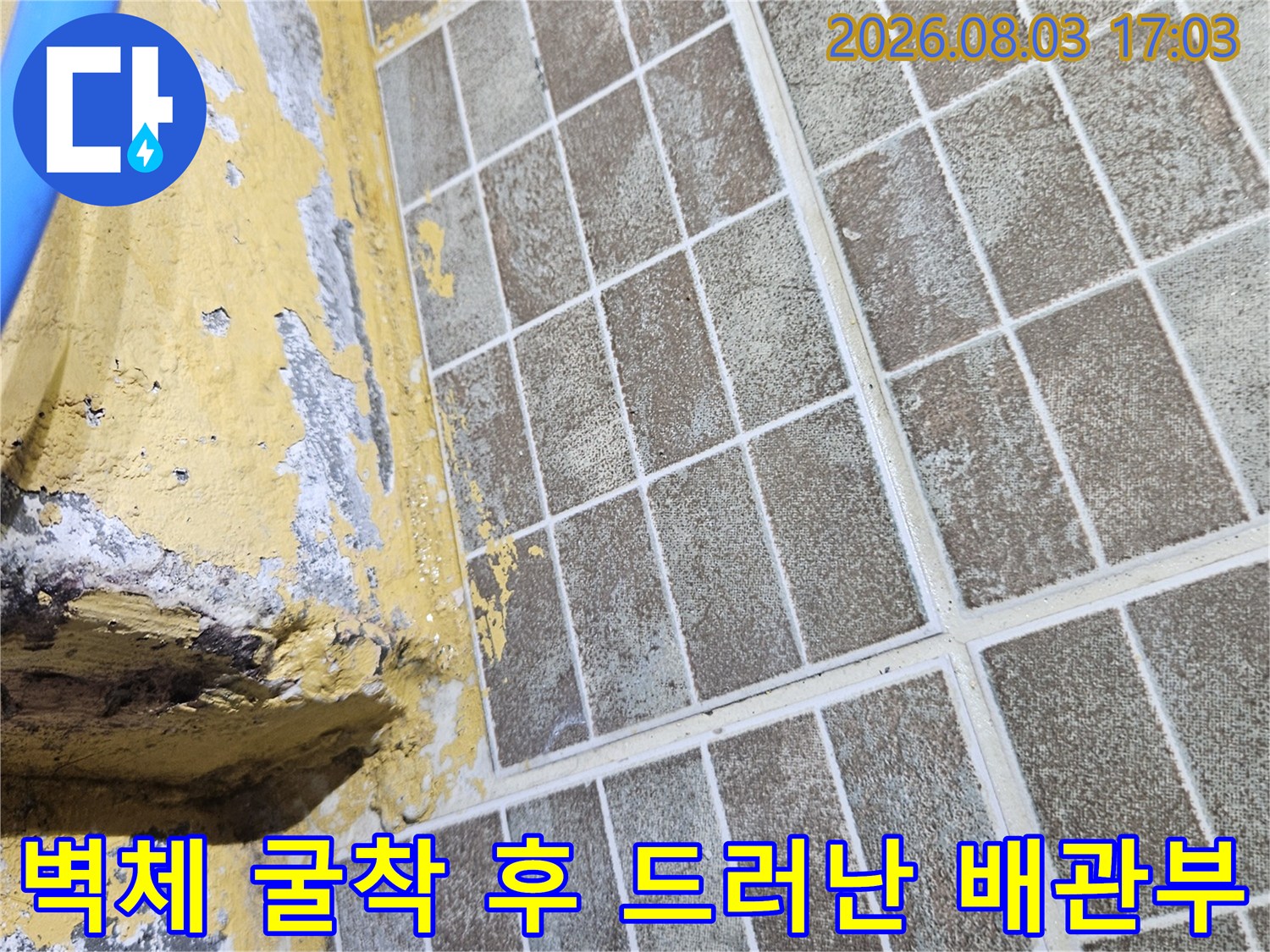 파손된 타일 벽면 뒤로 노출된 노란색 배관과 수선 구간