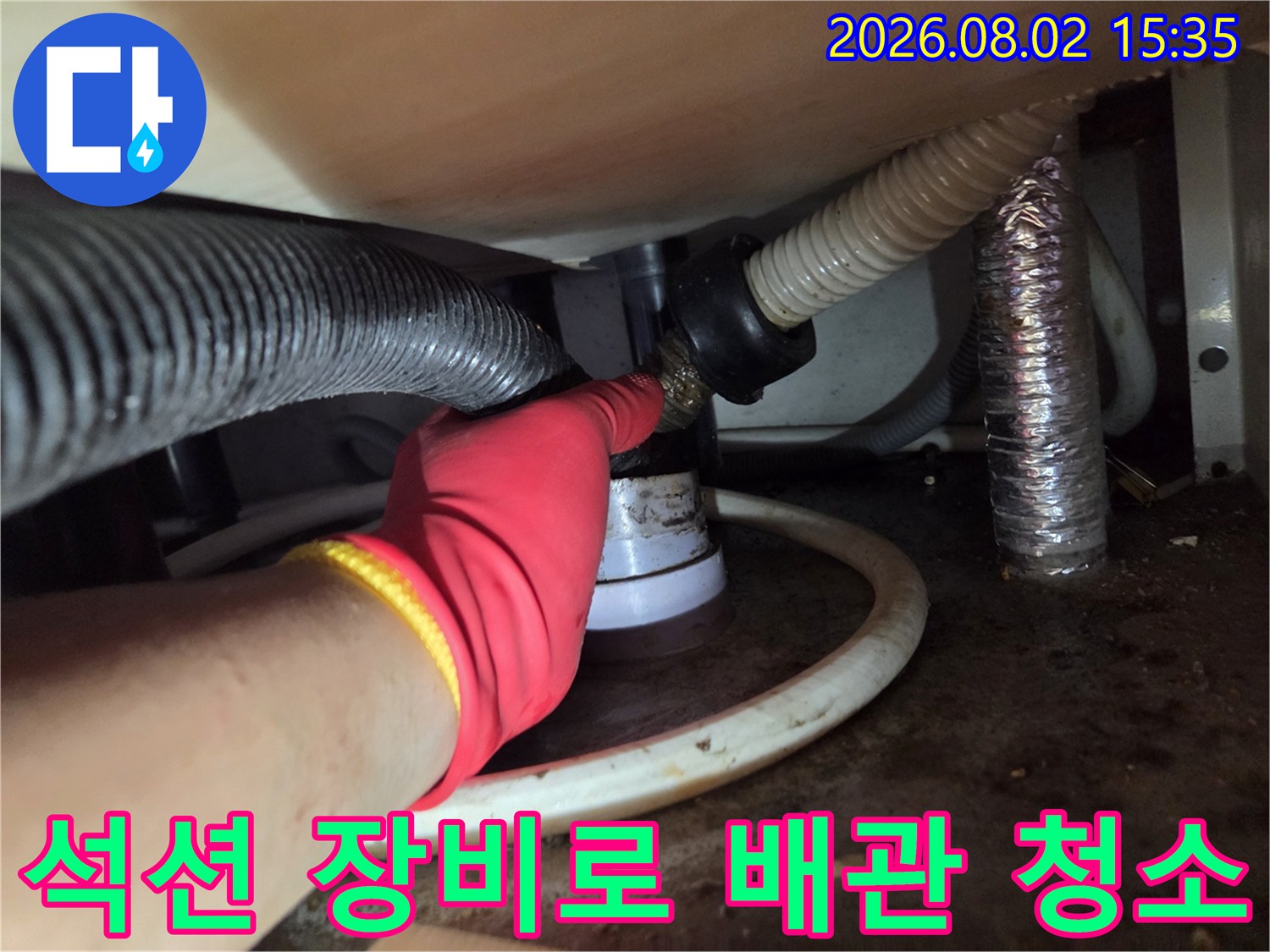 작업자가 싱크대 하단 트랩과 연결된 호스에 석션 기기를 연결하여 내부 이물질을 제거하는 모습