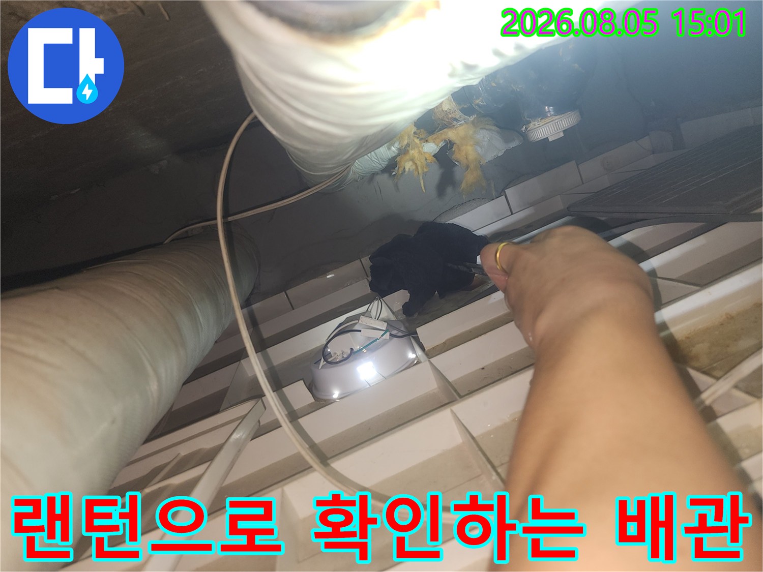 강력한 조명을 사용하여 천장 내부의 어두운 배관 부위를 조사하는 모습
