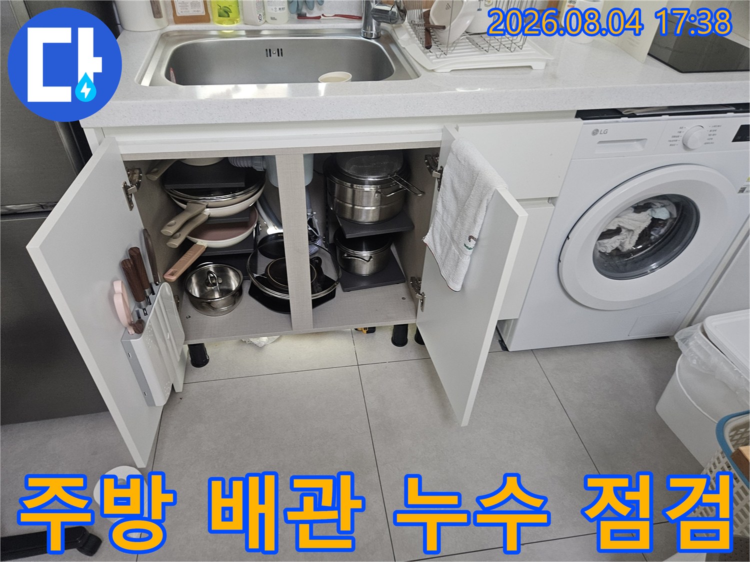 싱크대 아래를 열고 노출된 수도 배관의 상태와 연결 부위를 꼼꼼히 살피는 모습
