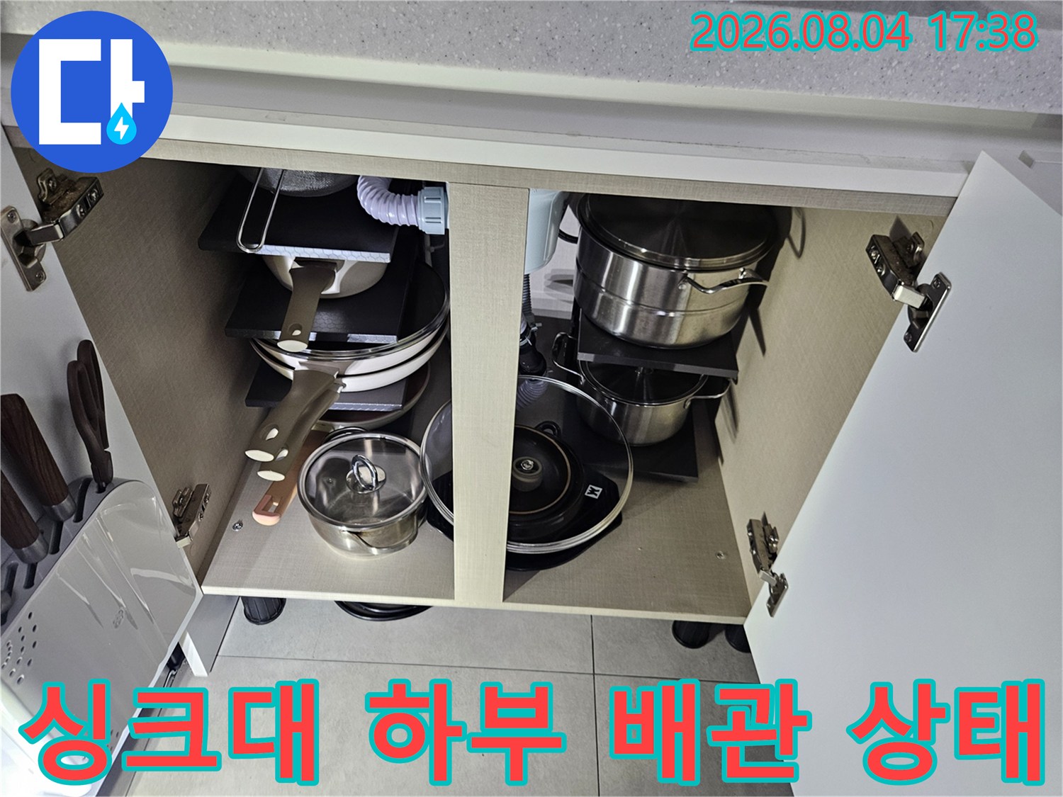 주방 싱크대 내부 공간에 놓인 물품들과 노출된 수도 배관들의 정밀 점검 모습
