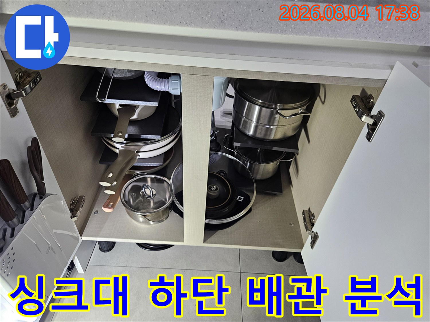 주방 싱크대 아래 수납 공간에 위치한 여러 개의 복잡한 온수 및 급수 배관을 정밀하게 진찰하는 장면입니다.