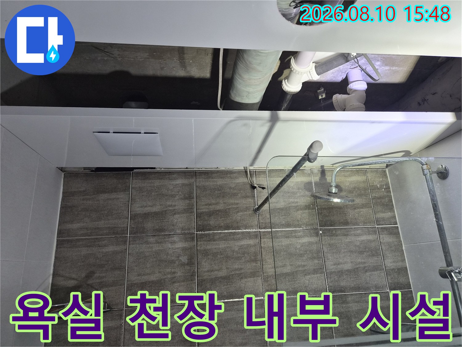 하수 배관과 샤워기 수전이 보이는-욕실 천장 내부 공사 현장입니다.