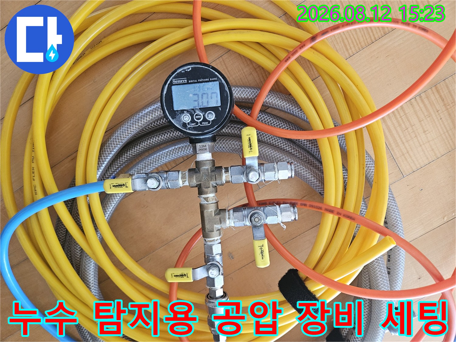 금속 밸브뭉치에 연결된 여러 색상의 호스와 디지털 측정기가 놓여 있는 모습