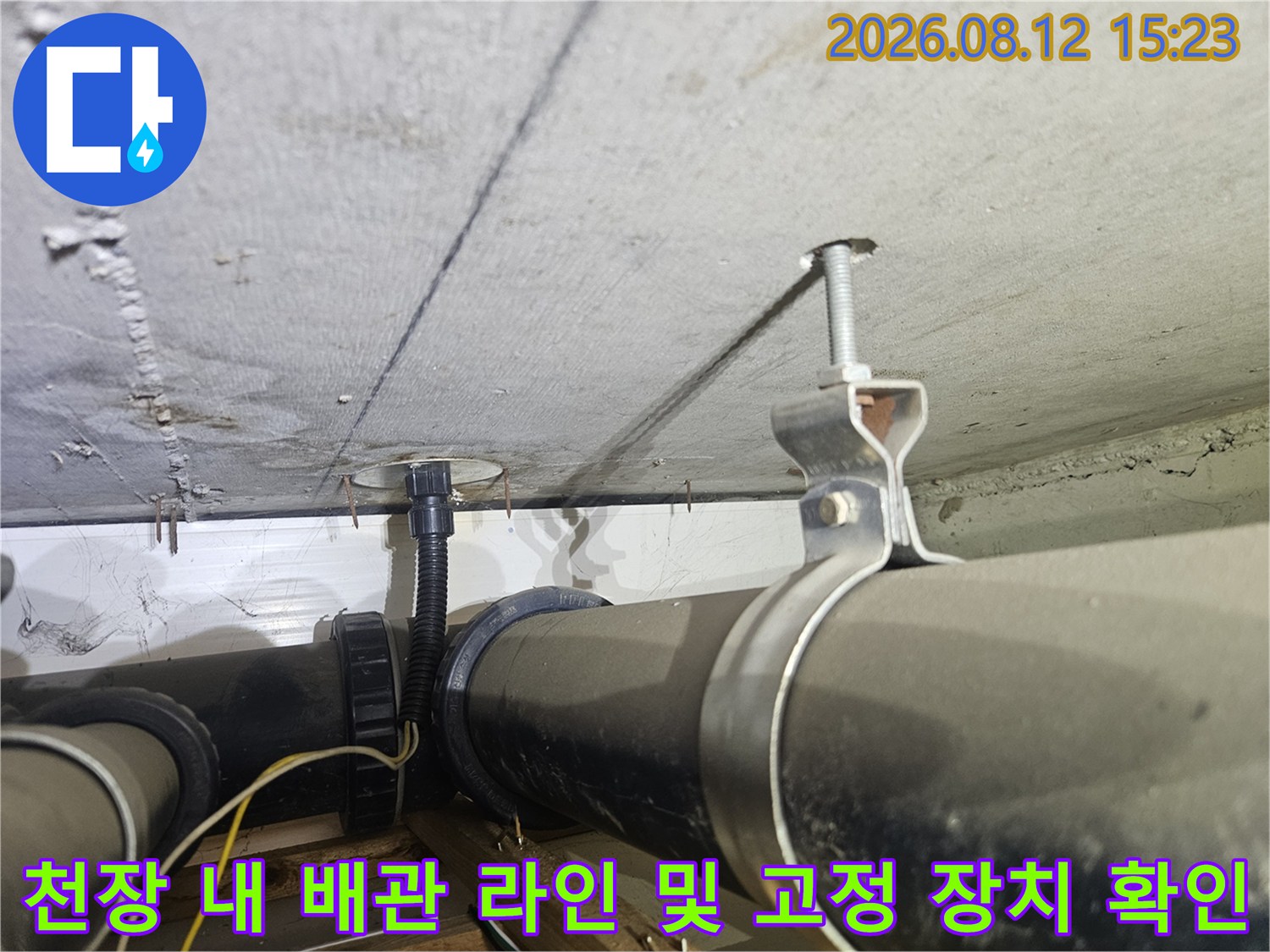 콘크리트 천장에 매달린 검은색 하수 관로-금속제 지지대와 전선 보호 주름관
