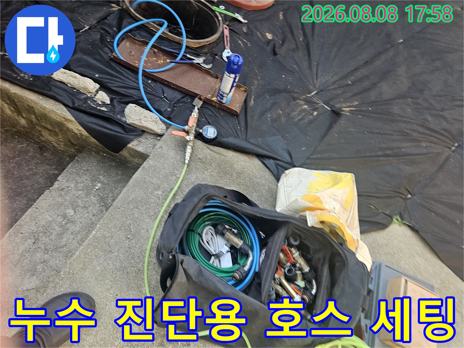 검은색 장비 가방과 파란색 압력 테스트용 호스가 놓여 있는 작업 현장