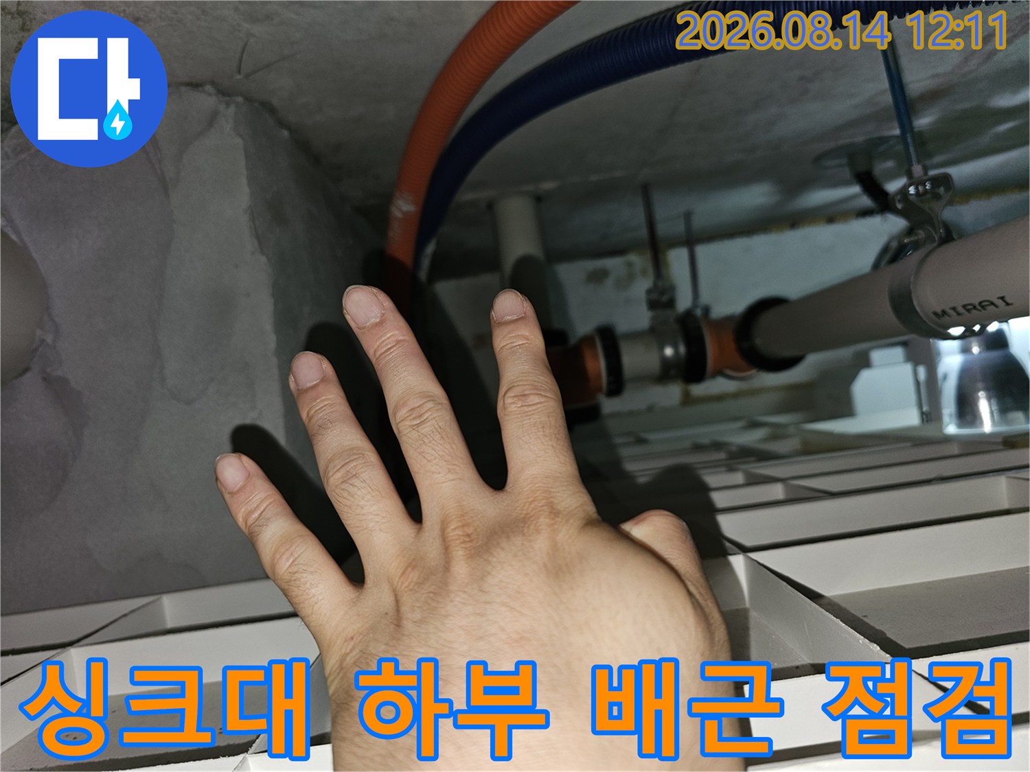 오렌지색과 파란색 주름관이 보이는 천장 내부를 손으로 가리키며 점검하는 사진입니다.