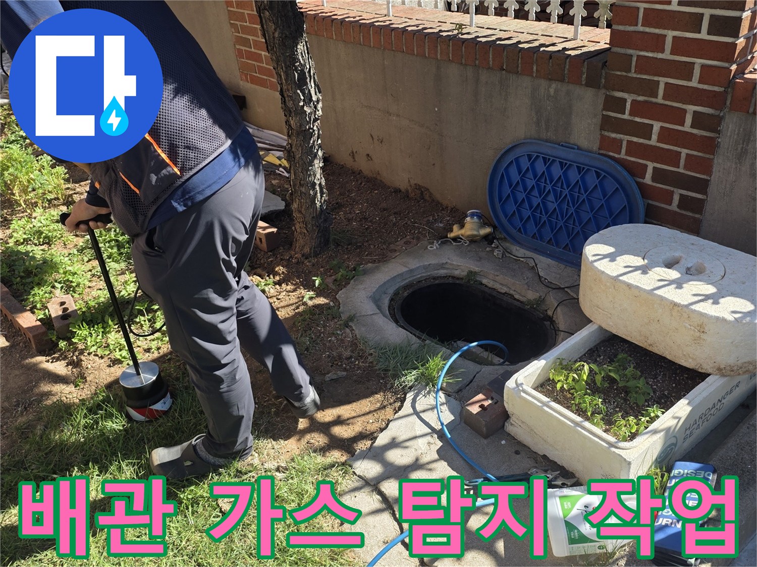 파란색 호스가 연결된-가스 탐지기로 지면의 누수를 추적하는 장면입니다.