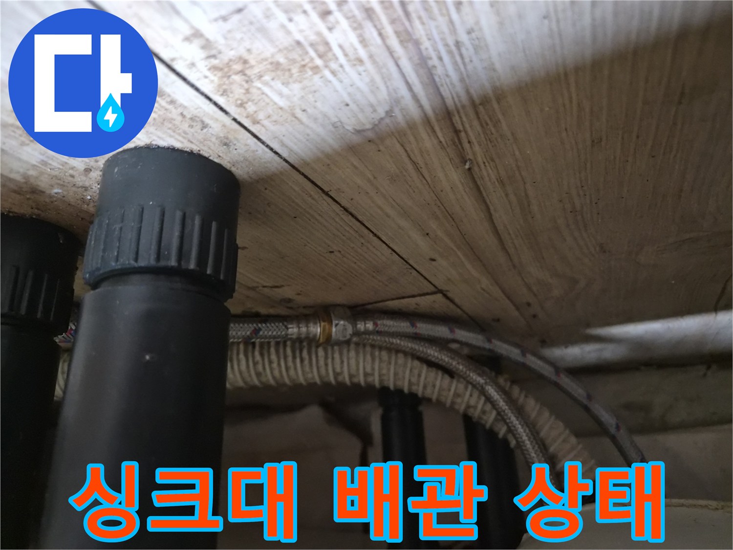 싱크대 하부장 내부의 검은색 배관과 은색 호스 연결 부위 모습