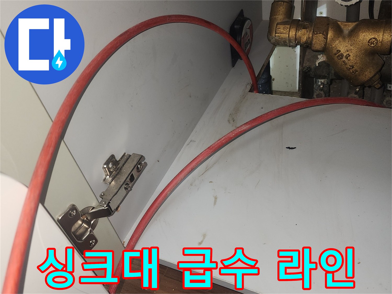 금속 재질의 밸브와 붉은색 호스가 보이는 싱크대 하부 모습