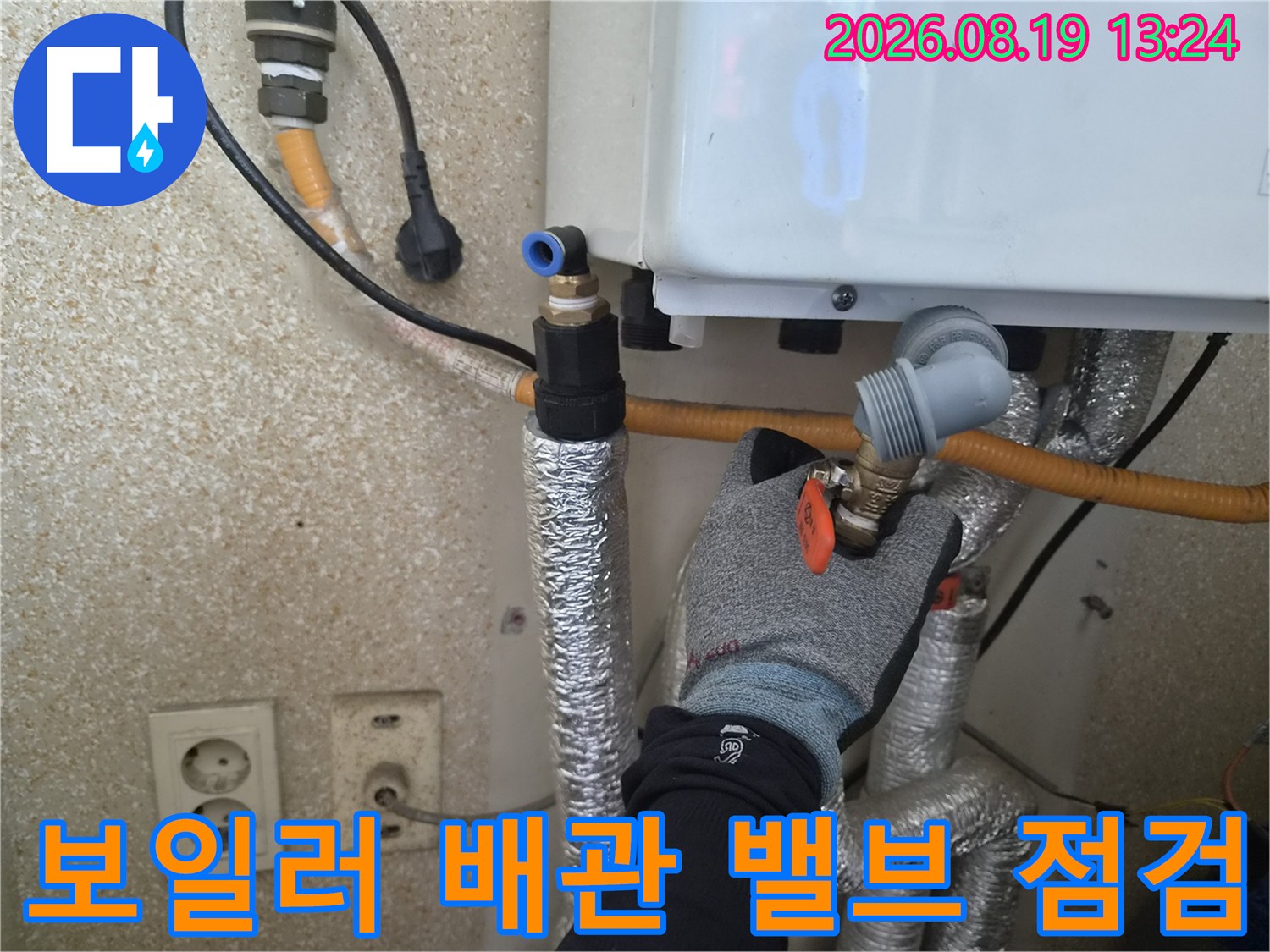 작업자가 보일러 하단의 금속 밸브와 노란색 호스 연결부를 면밀히 보고 있습니다.