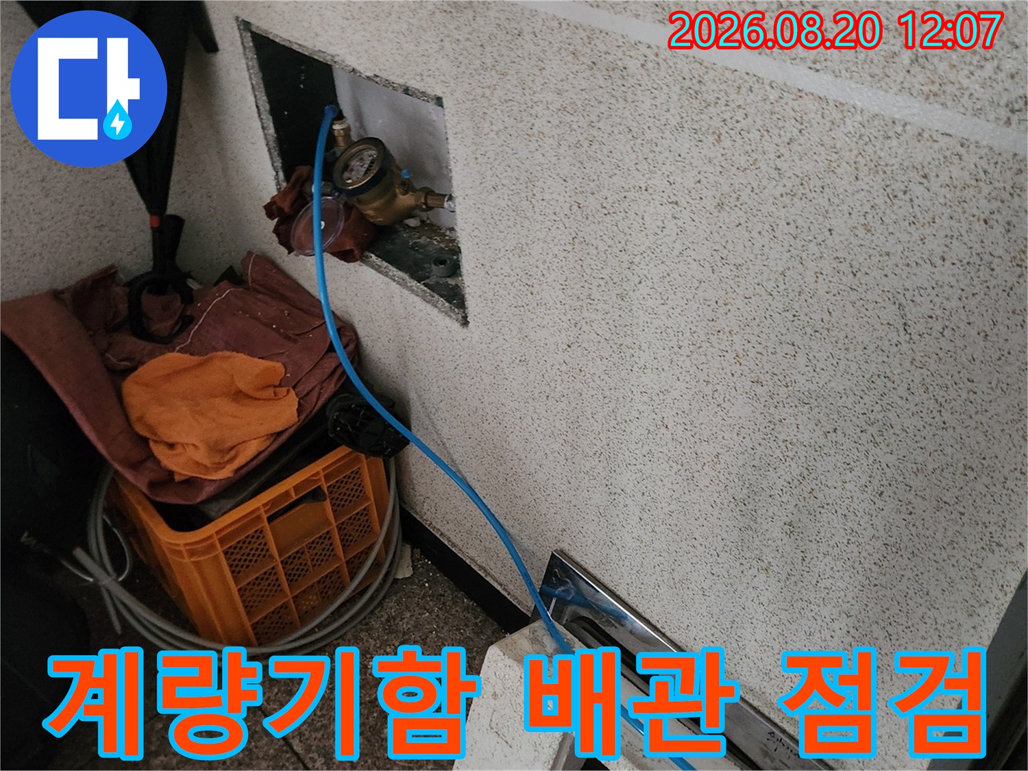 타일 벽면 안쪽에 설치된 수도 계량기와 검사 장비의 모습입니다.