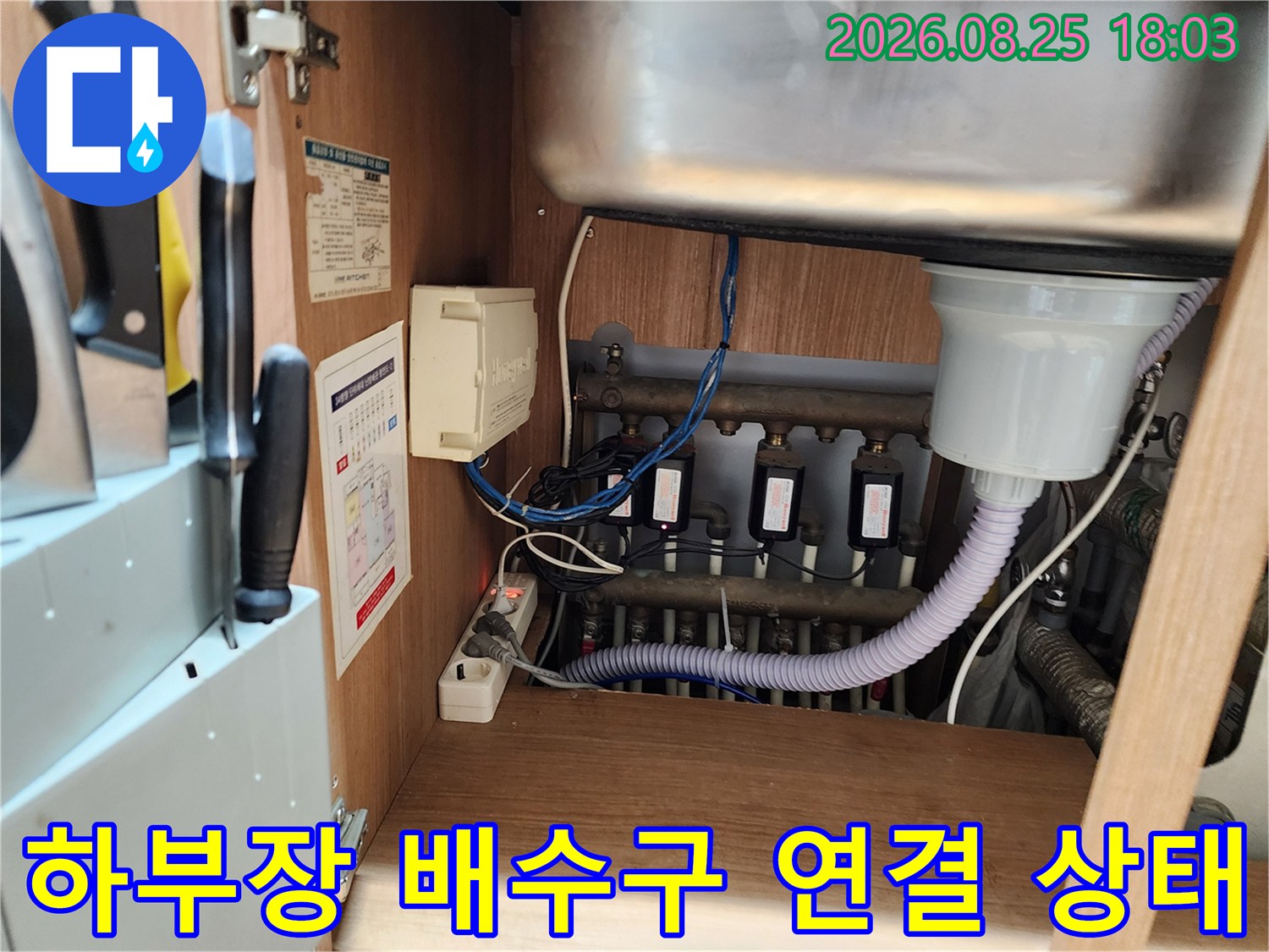 싱크대 하부장 내부에 위치한 굵은 흰색 배수 호스와 분기된 검은색 배관들