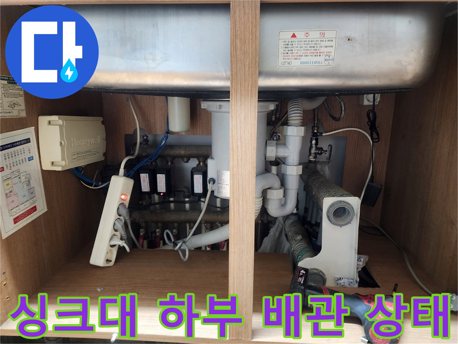 주방 싱크대 아래쪽의 복잡한 배수관 연결 부위와 호스 모습