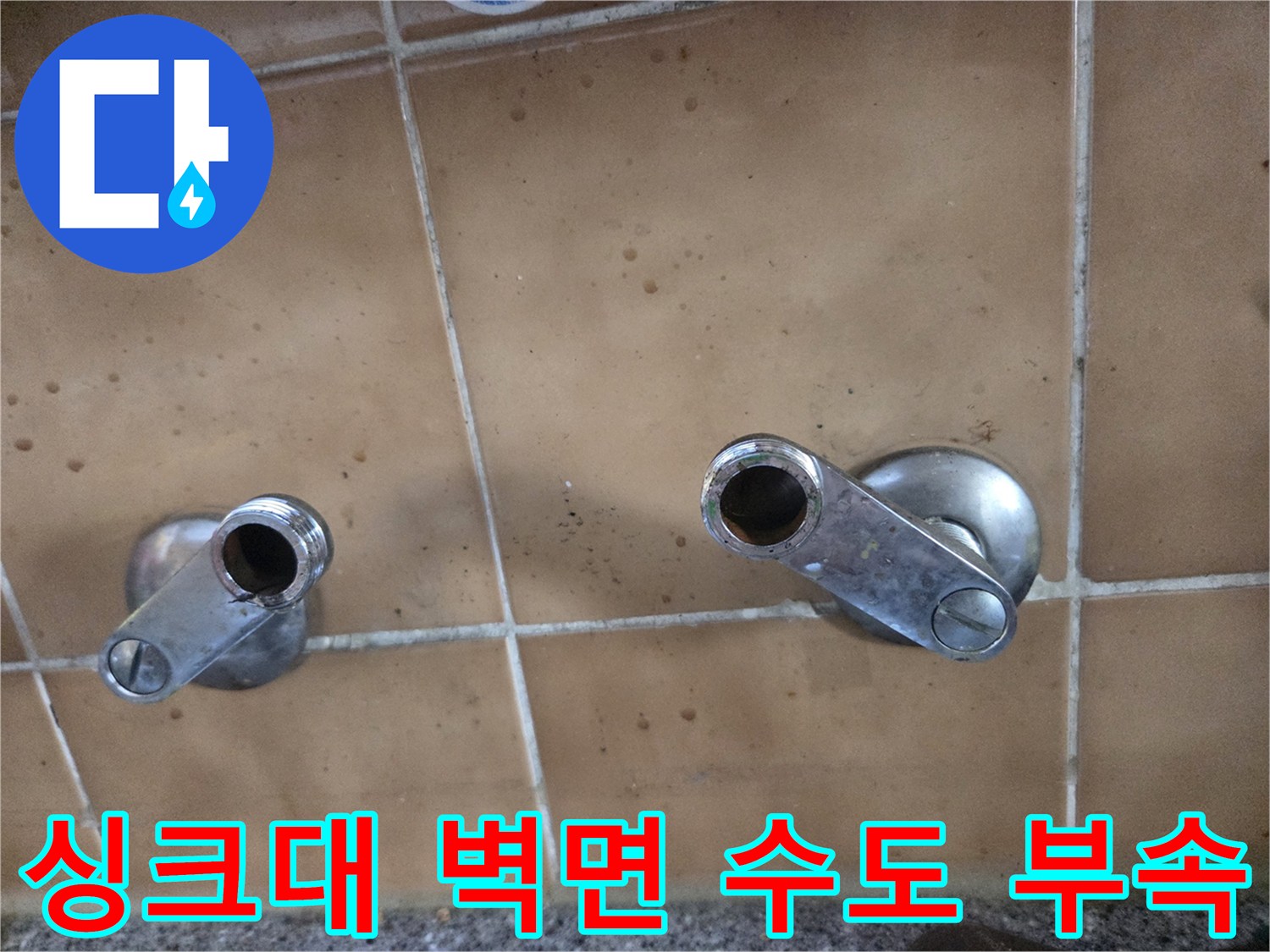 싱크대 타일 벽면에 위치한 은색 매립형 수전 연결 부위 사진입니다.