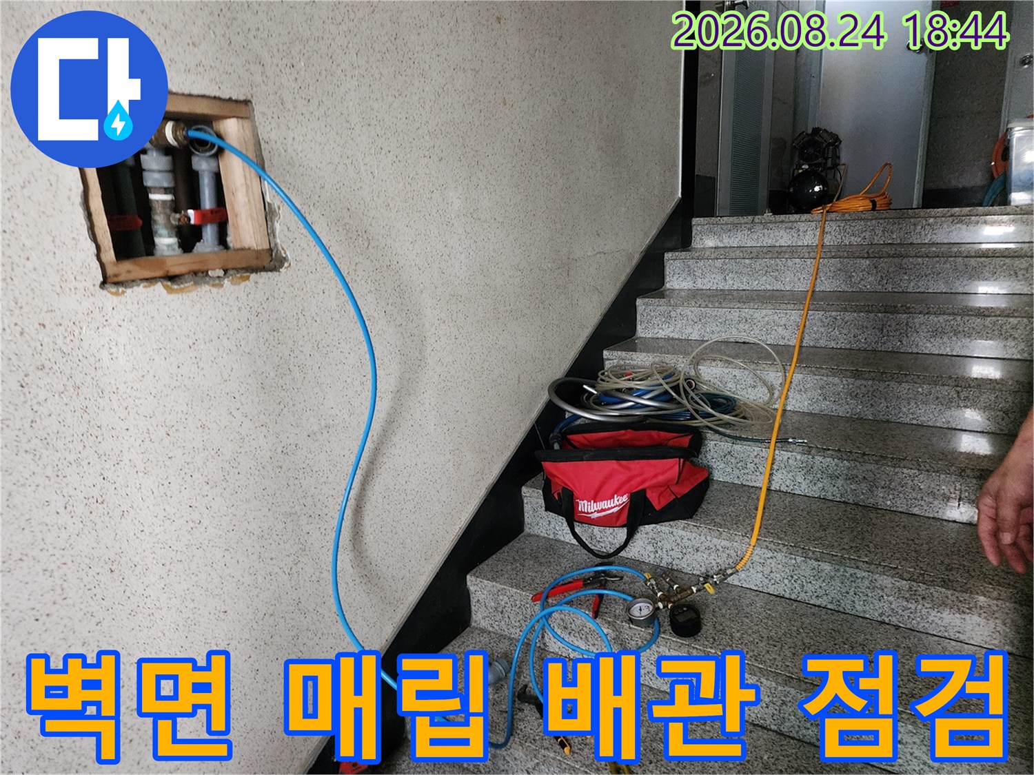 벽체에 노출된 흰색 배관 부위와 연결된 압력 측정용 호스 모습입니다.