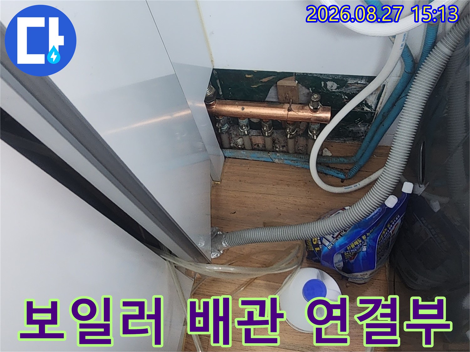 싱크대 아래쪽 보일러 분배기와 굵은 호스들이 복잡하게 연결된 현장 사진입니다.