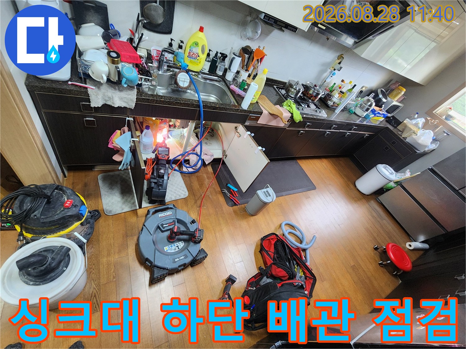 주방 싱크대 아래 공간에서 배관 연결 상태를 면밀히 조사하는 작업 모습입니다.