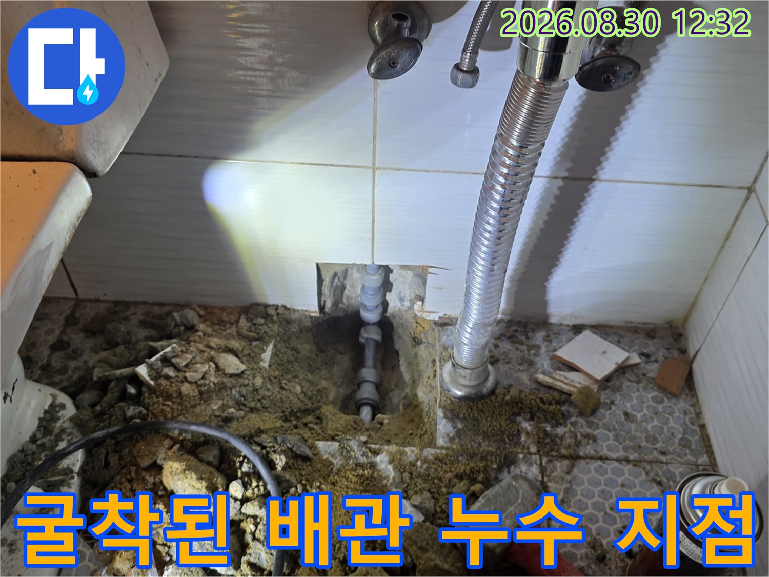 타일을 제거하고 드러난 젖은 흙과 노출된 배관의 상태를 보여줍니다.