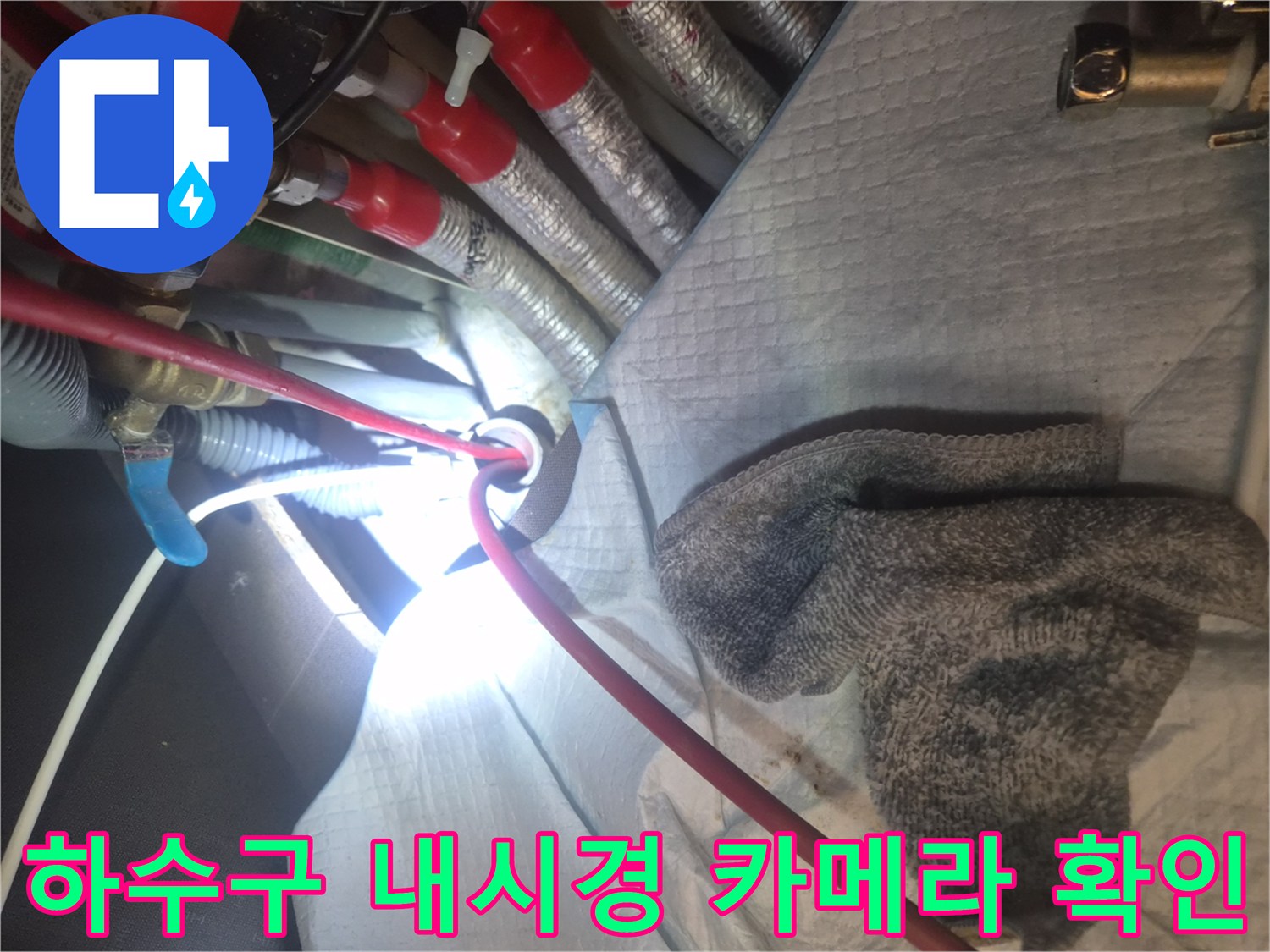싱크대 하단 배관 입구에 내시경 장비를 삽입하여 내부를 보는 장면입니다.