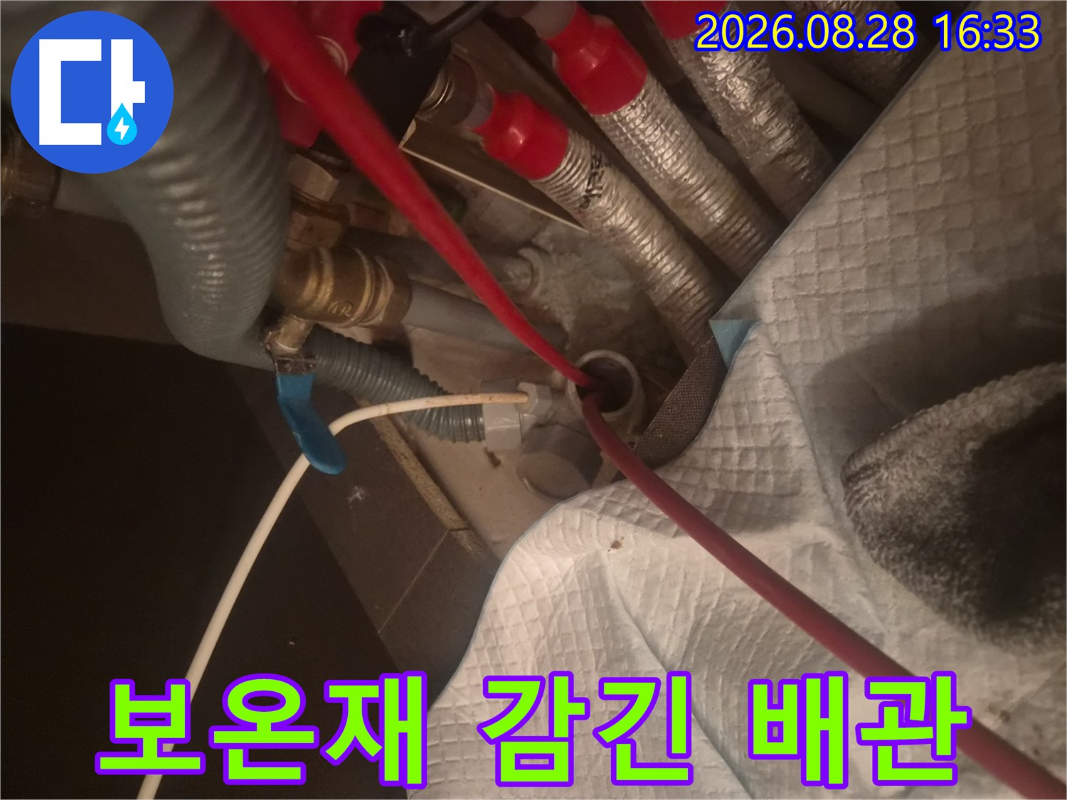 은색 보온재와 붉은 마감재로 정돈된 배관 연결 부위입니다.