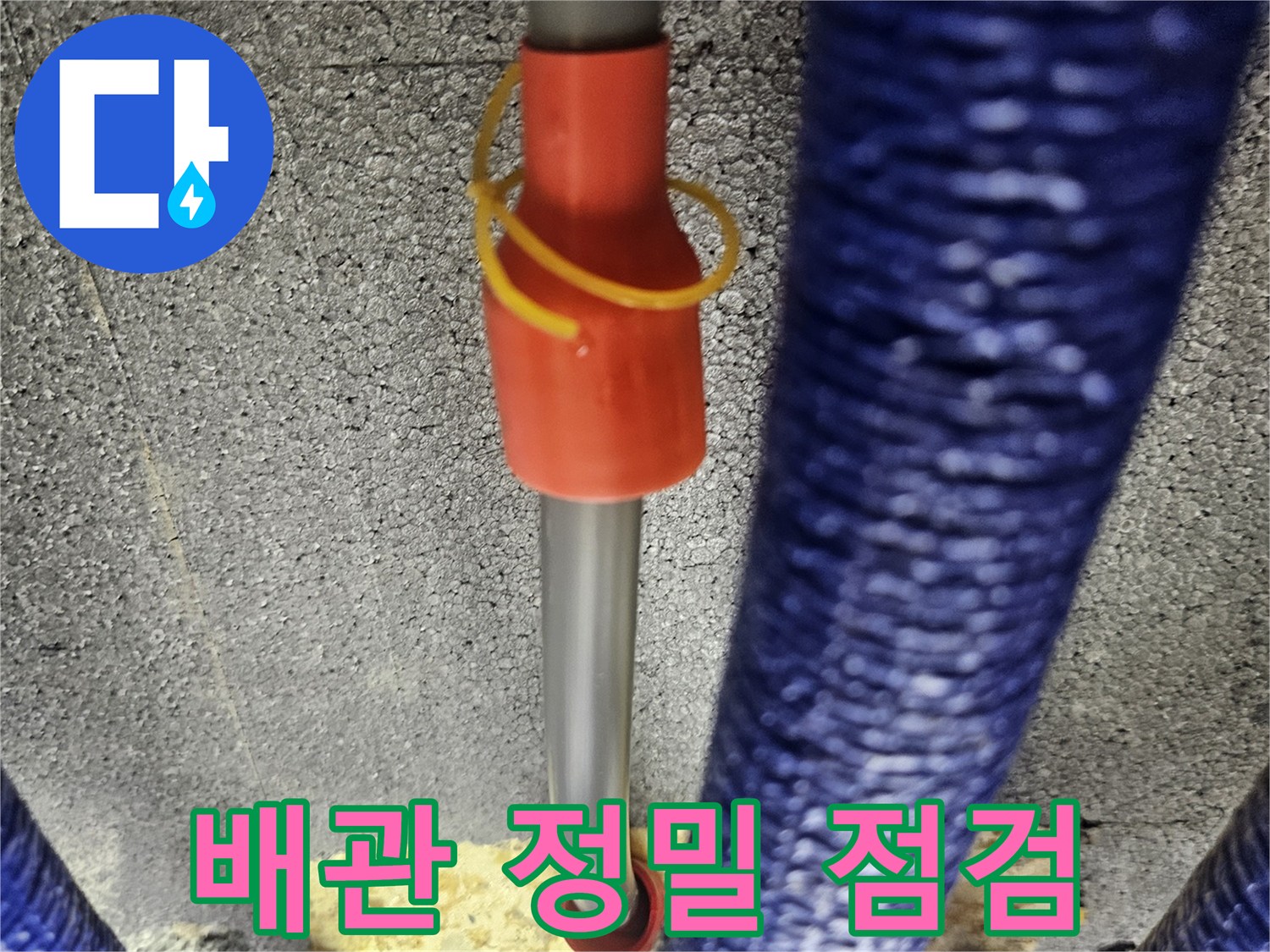 벽면 틈새로 내시경 카메라를 넣어 파란색 보온재가 감긴 배관을 조사하는 모습입니다.