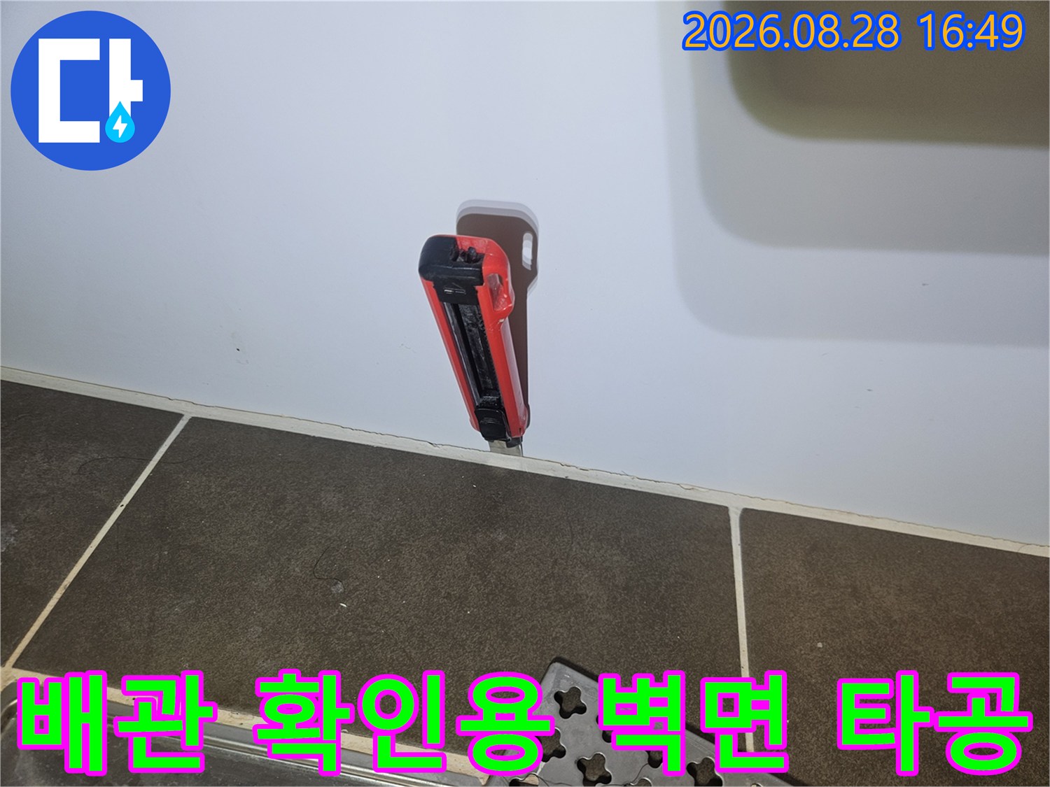 타일 벽면을 뚫어 내부 배관의 이상 유무를 점검하고 있는 현장 사진입니다.