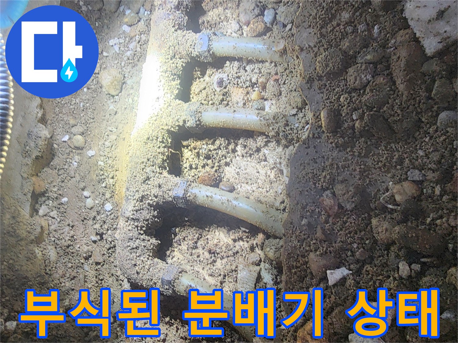 싱크대 아래 흙과 자갈 사이에 드러난 부식된 금속 배관 분배기