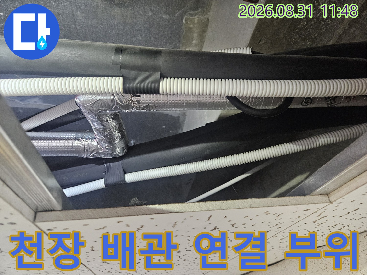 하얀색 주름관과 은색 보온재가 겹쳐져 있는 천장 내부 배관 모습입니다.