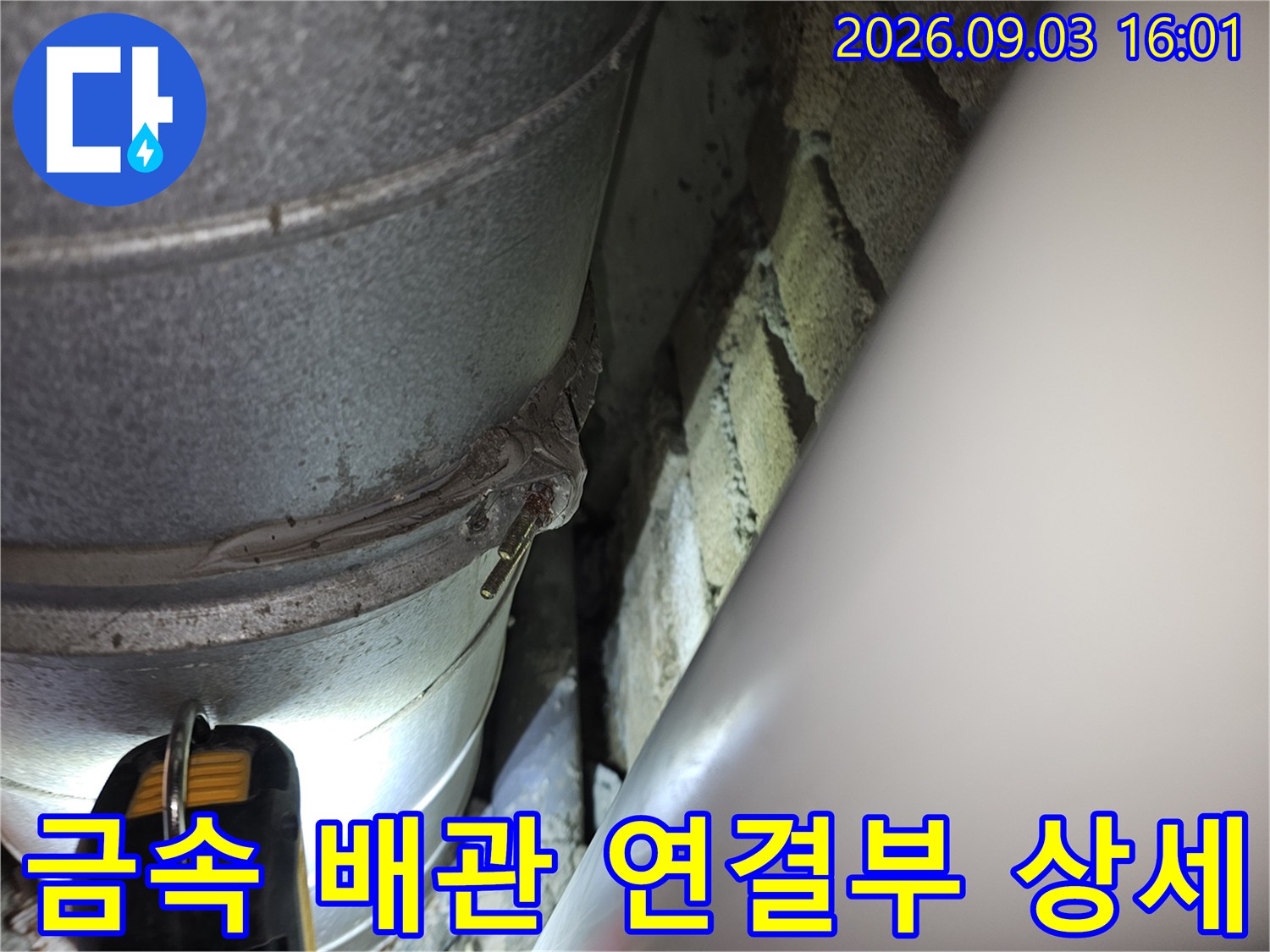 두꺼운 금속 배관과-벽면 사이의 접합부를 근접 촬영하였습니다.