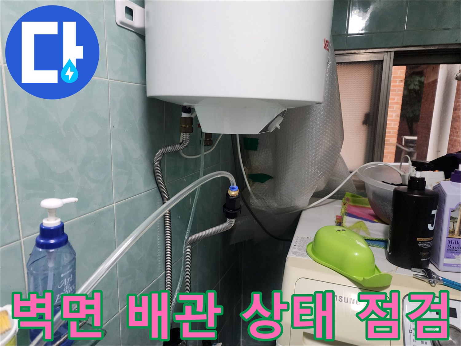 타일 벽면에 설치된 수도 배관과 연결 호스를 점검하는 장면입니다.