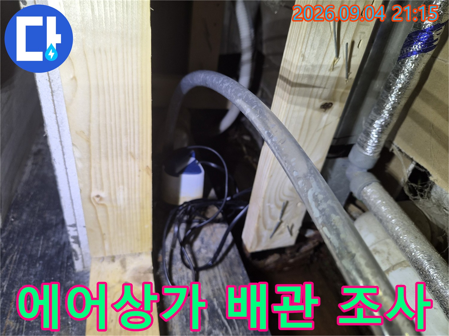 목재 지지대 사이로 노출된 에어컨 드레인 호스와 보온 배관