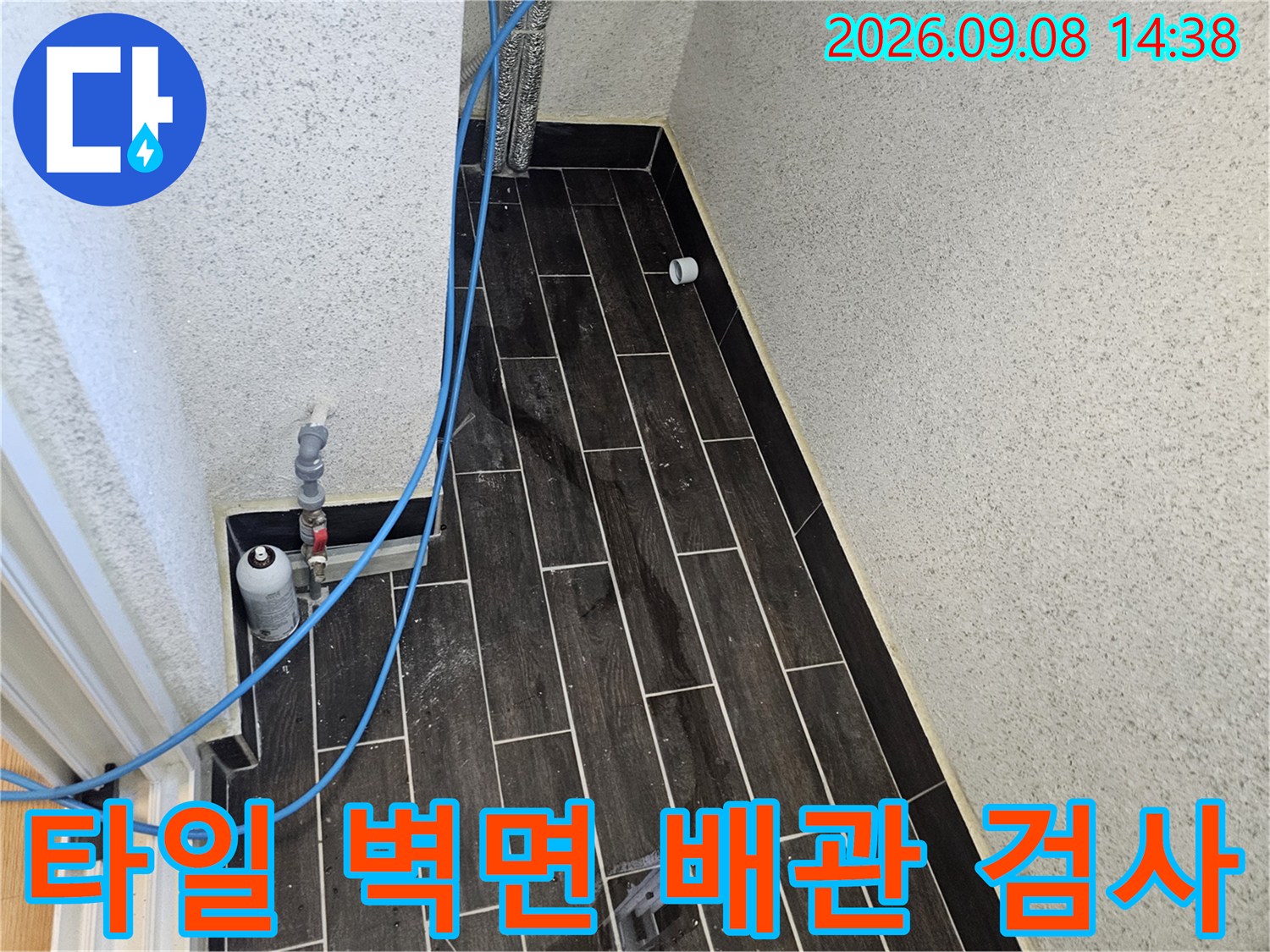 어두운 타일 벽에 연결된 파란색 호스와 압력 측정 장치 상세