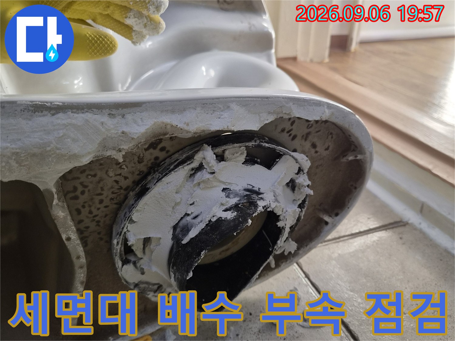 세면대 하부의 검은색 배수 부속과 주변의 백시멘트 잔해 사진입니다.