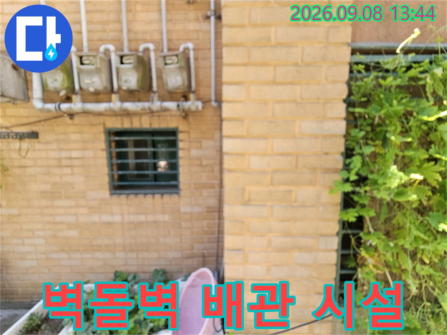 벽돌로 된 외벽에 나란히 배치된 수도 계량기와 흰색 배관입니다.