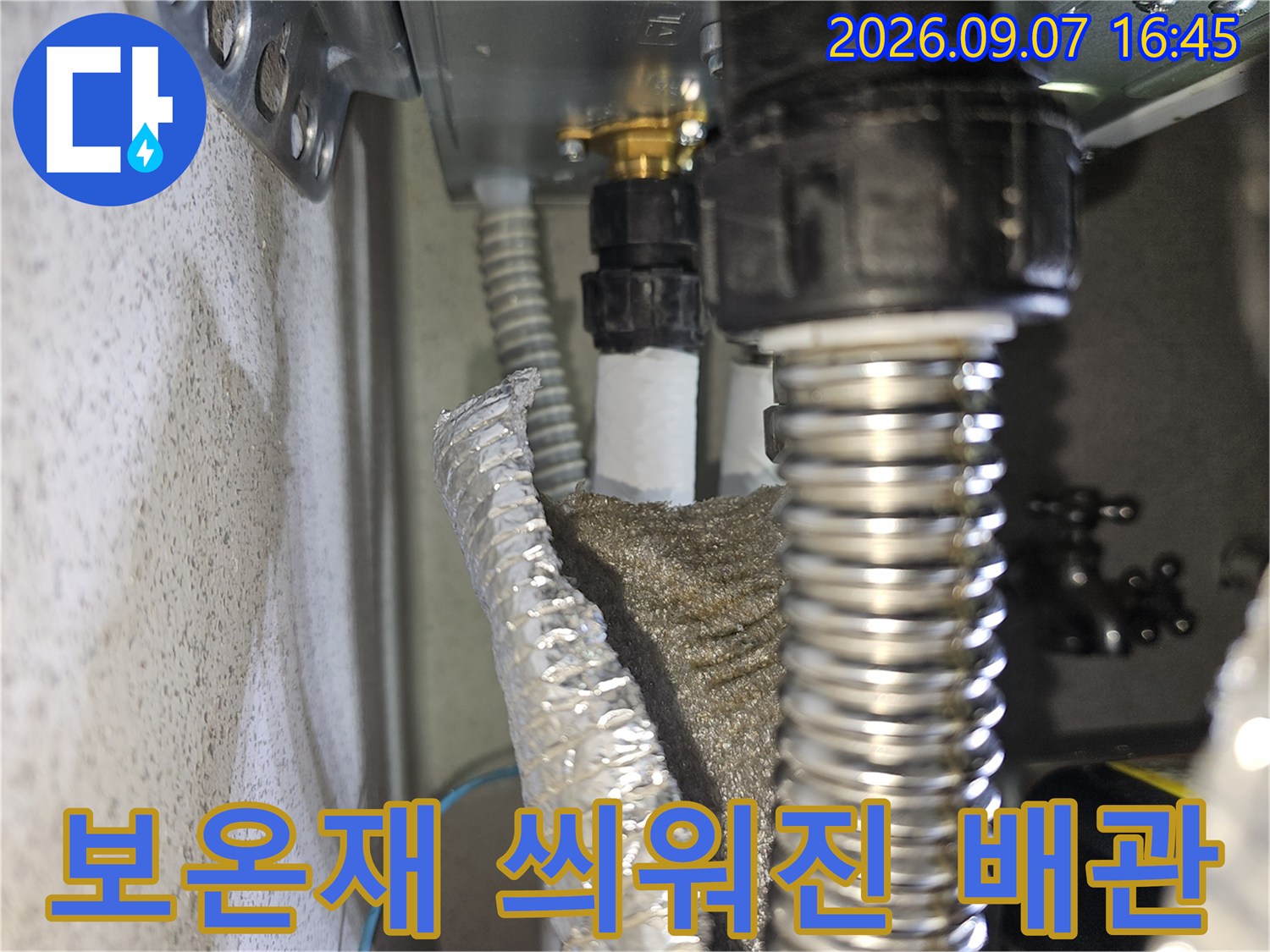 하얀색 보온재와 은색 주름관이 연결된 천장 설비의 모습입니다.