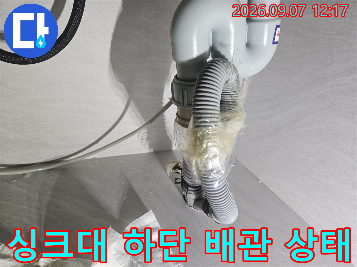 싱크대 밑 공간에-테이프로 고정된 훼손된 호스와 배관의 모습입니다.