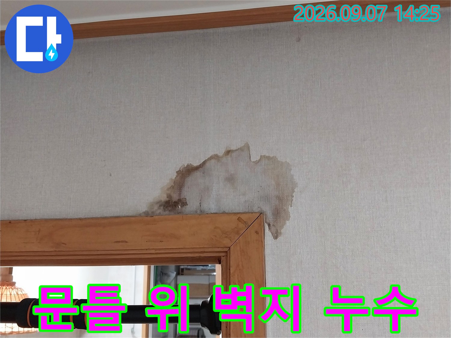 나무 문틀 상단에 나타난 젖은 벽지와 갈색 얼룩 사진입니다.