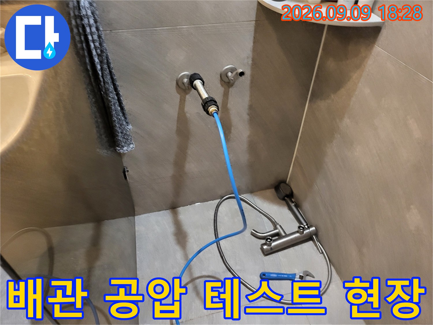 벽면 배관 연결 부위에 파란색 호스와 압력 측정 장치를 설치한 모습입니다.