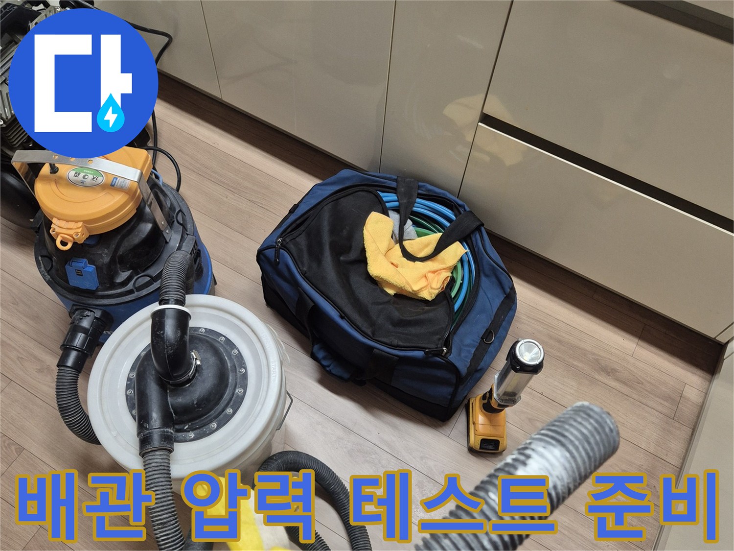 싱크대 아래쪽 바닥면에서 진행 중인 배관 공압 테스트 장비와 청소 도구들